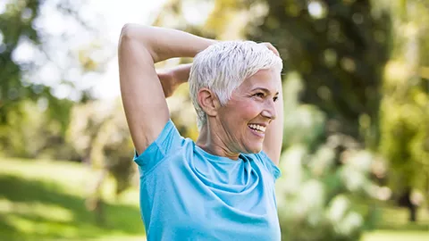 older woman stretching and smiling outdoors